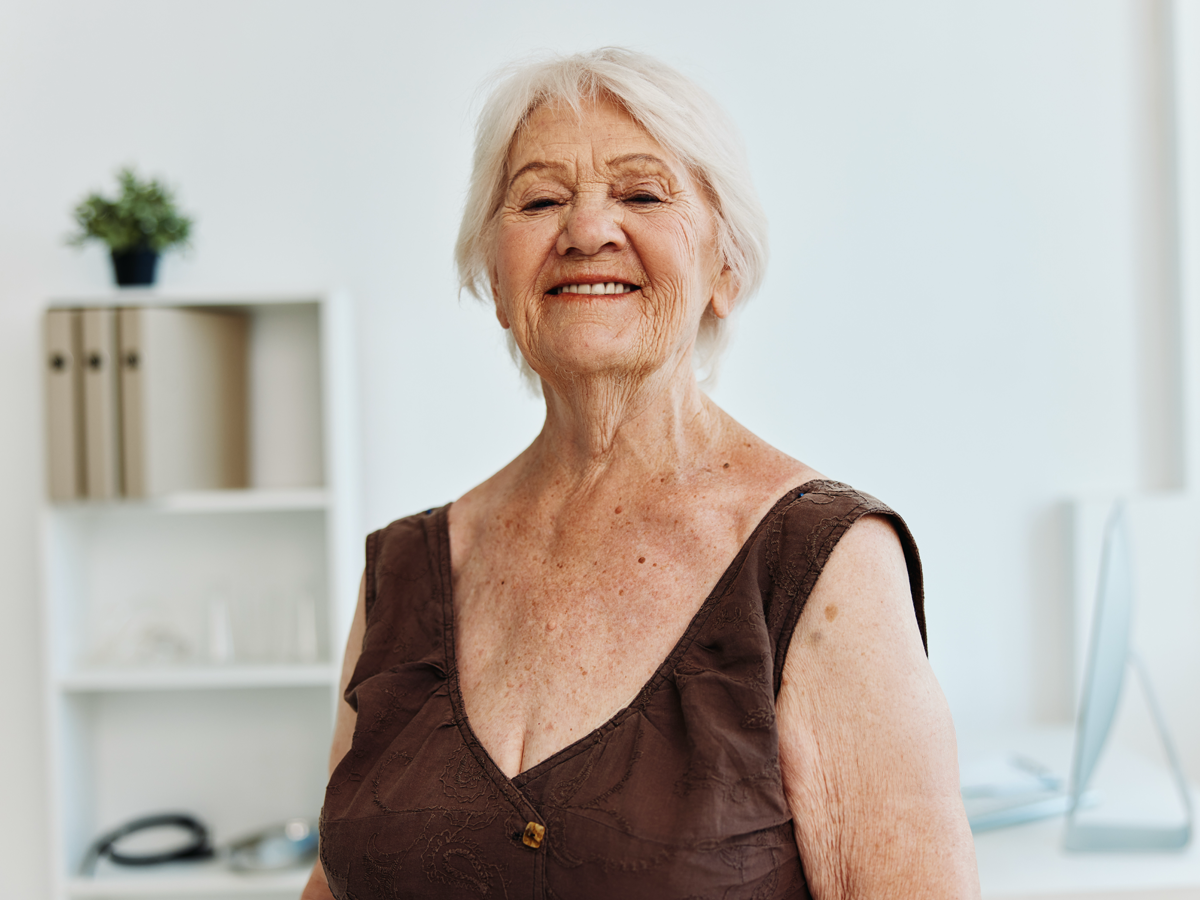 Older woman smiling in a bright, modern interior with soft natural light and clean neutral decor.