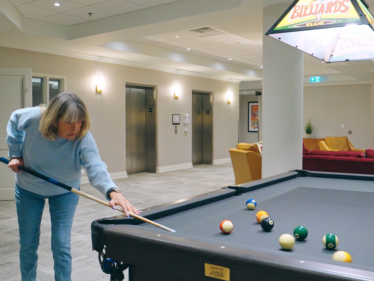 Resident playing billiards in a bright games room with casual lounge seating nearby.