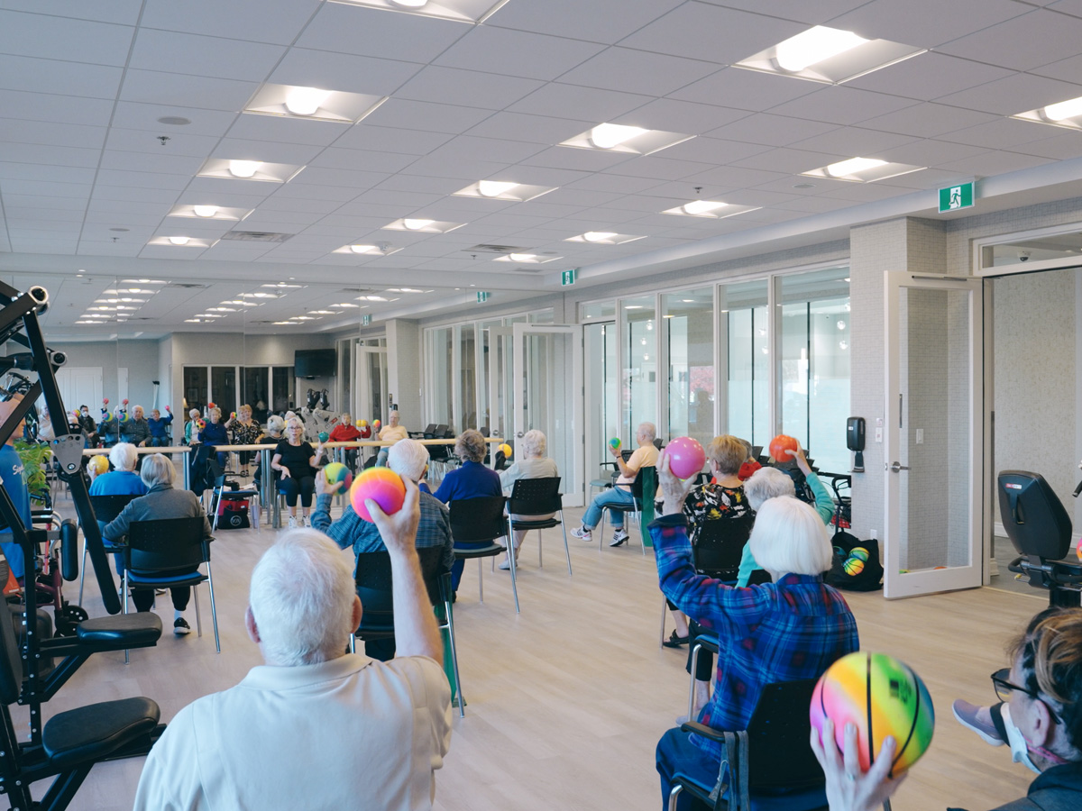 Group fitness class in a bright studio with residents participating in guided exercise.