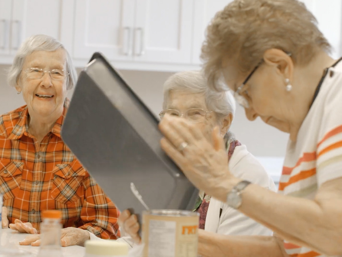 Residents gathered around a table during a group activity in a bright communal kitchen space.